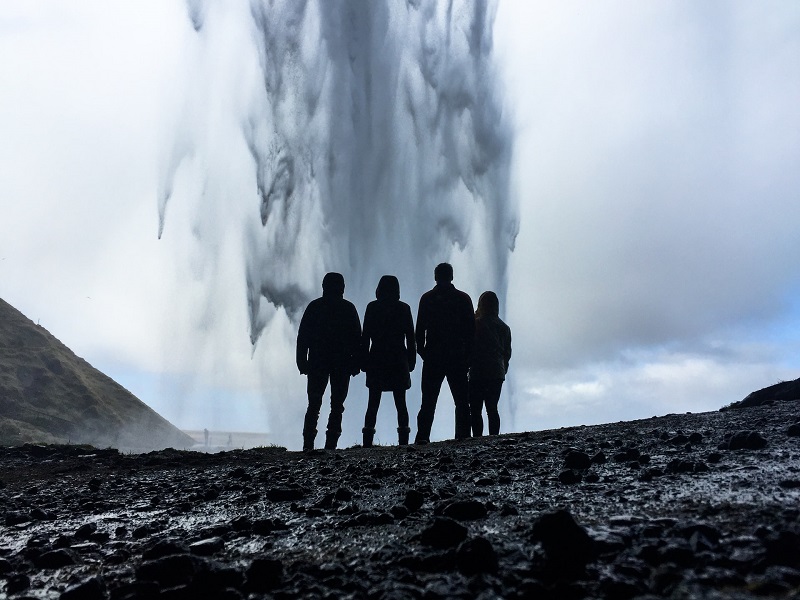 four people standing next to a waterfall 